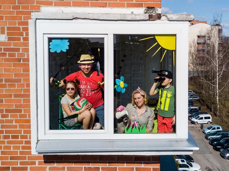 Das Foto zeigt eine Familie, die sich hinter einem Fenster ihrer Wohnung versammelt hat und sich offenbar von der Coronapandemie nicht unterkriegen lässt.