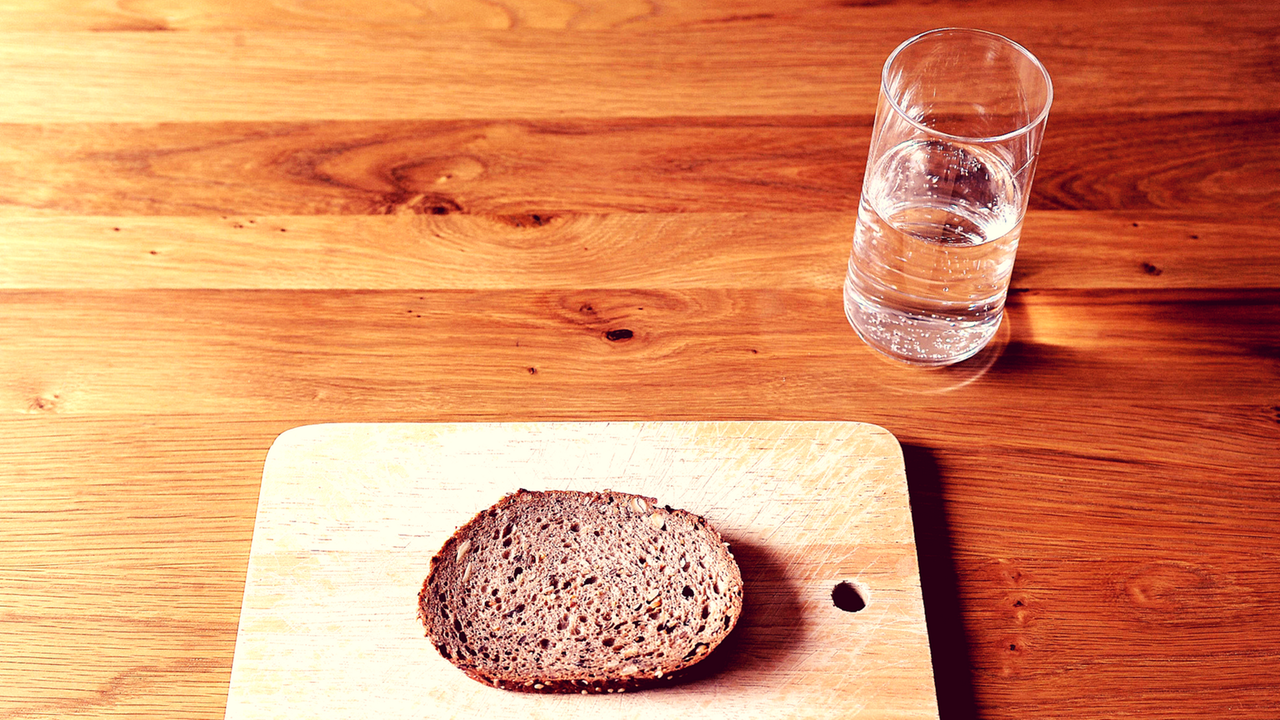 Eine Scheibe Brot und ein Glas Wasser stehen auf einem Tisch. Eine Scheibe Brot und ein Glas Wasser stehen auf einem Tisch.