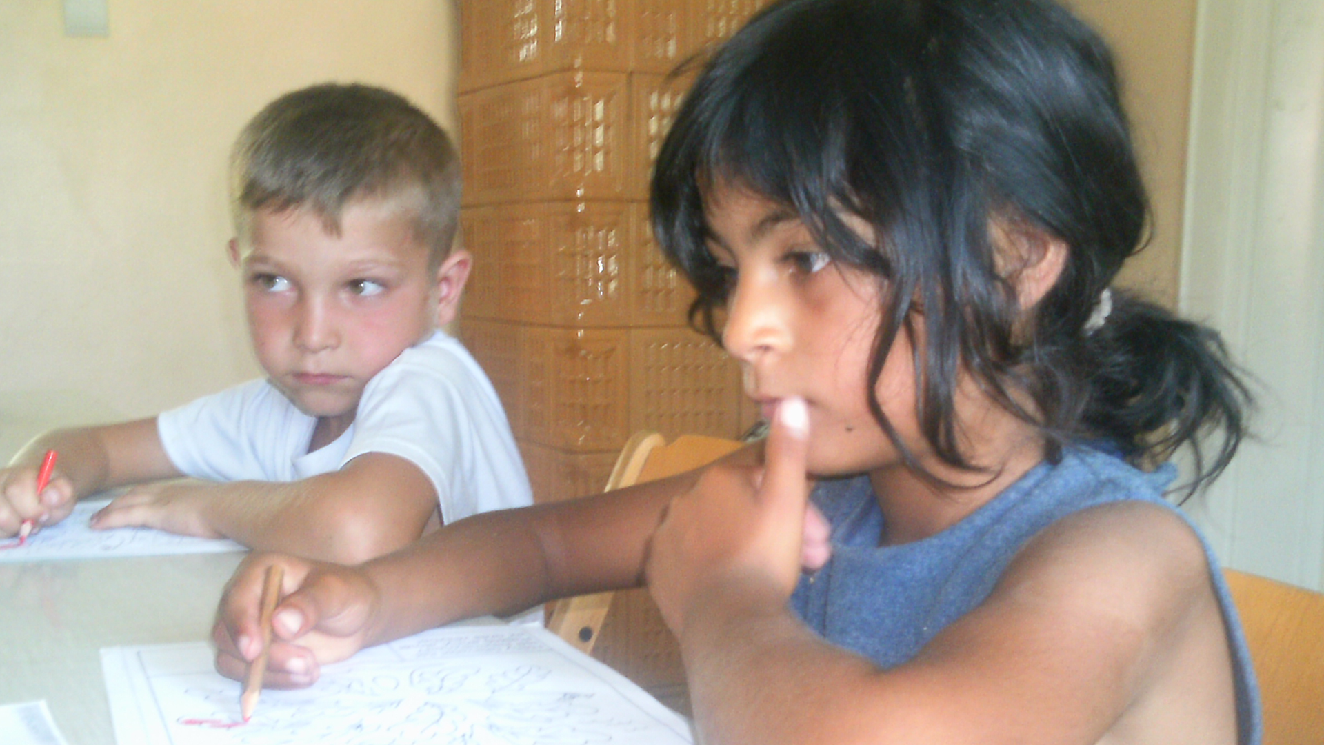 Ein Mädchen und ein Junge sitzen schreibend an einem Schultisch. 