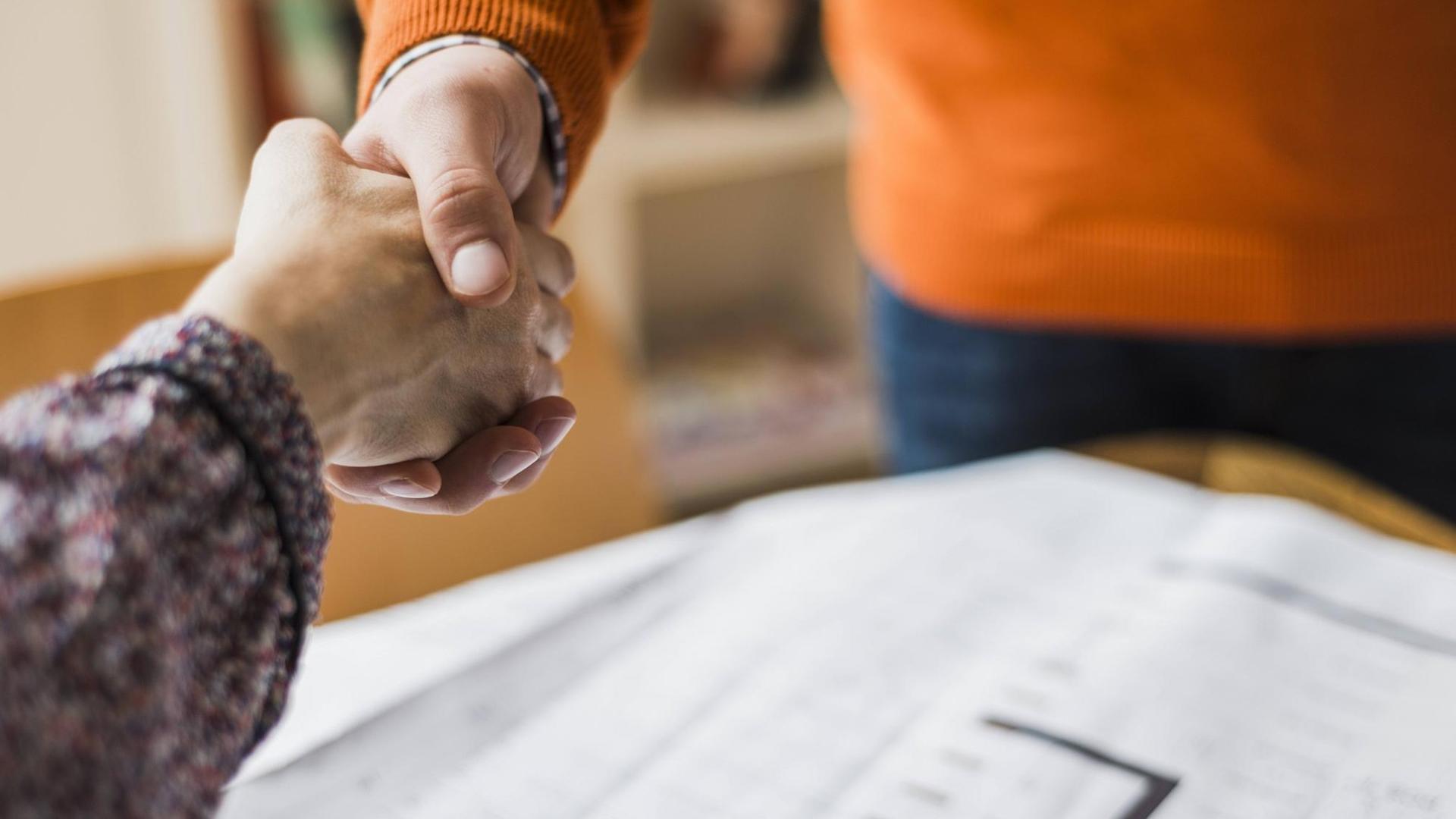 Farbfoto, Nahaufnahme, Handschlag zwischen Mann und Frau über einem Plan, Symbolfoto Farbfoto, Nahaufnahme, Handschlag zwischen Mann und Frau über einem Plan, Symbolfoto