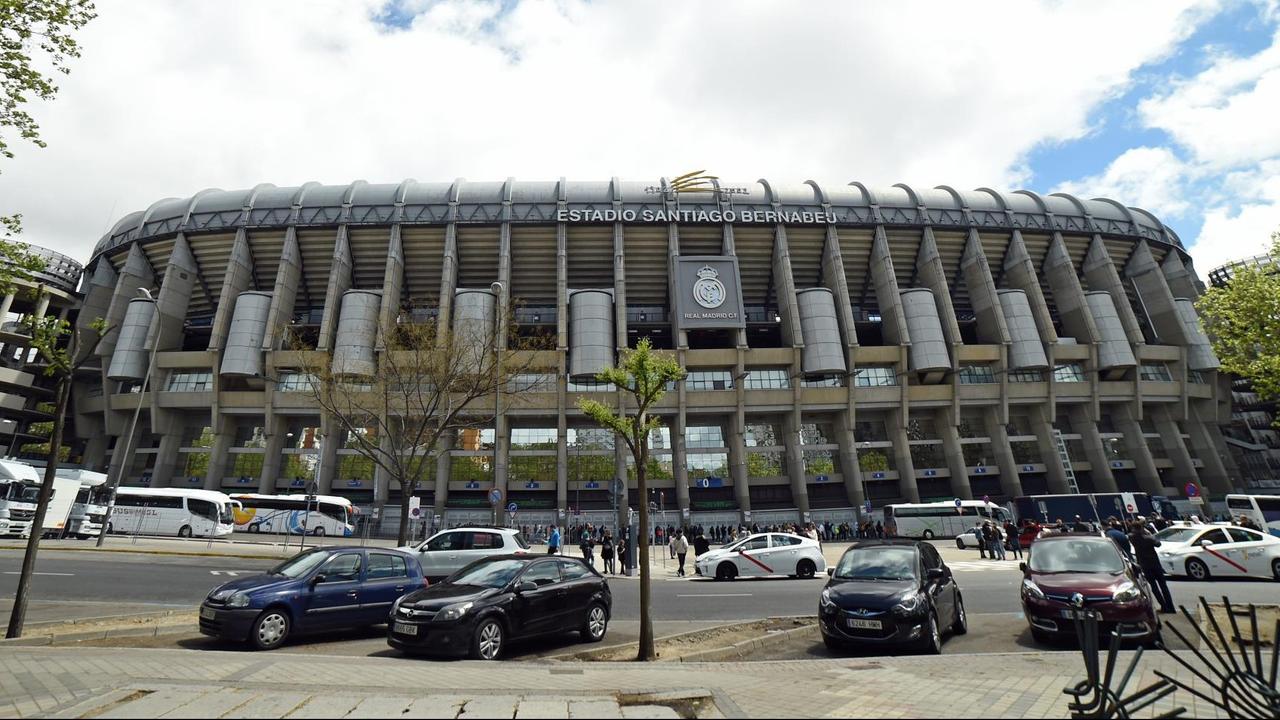 Blick auf das Stadion und einen Parkplatz davor unter bewölktem Himmel. Vor dem Stadion stehen viele Menschen. Blick auf das Stadion und einen Parkplatz davor unter bewölktem Himmel. Vor dem Stadion stehen viele Menschen.