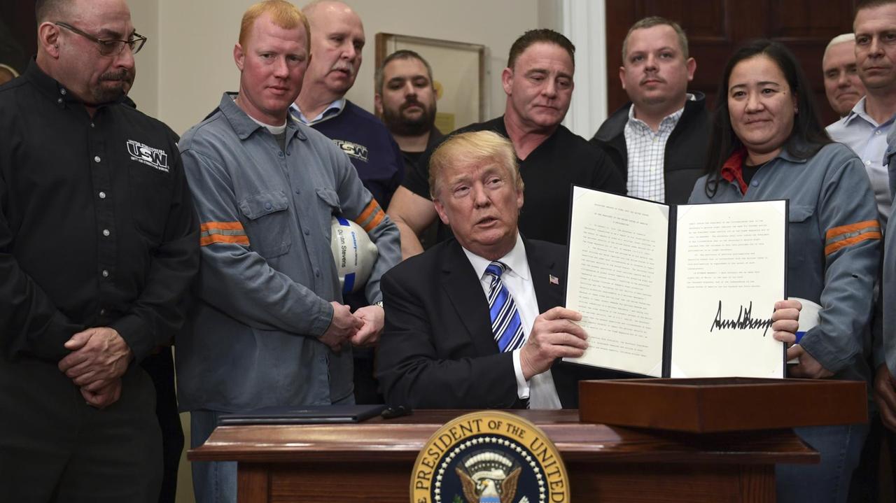 Das Bild zeigt US-Präsident Trump nach der Unterzeichnung seiner Verordnung über Schutzzölle. Er ist umringt von amerikanischen Stahlarbeitern. Das Bild zeigt US-Präsident Trump nach der Unterzeichnung seiner Verordnung über Schutzzölle. Er ist umringt von amerikanischen Stahlarbeitern.