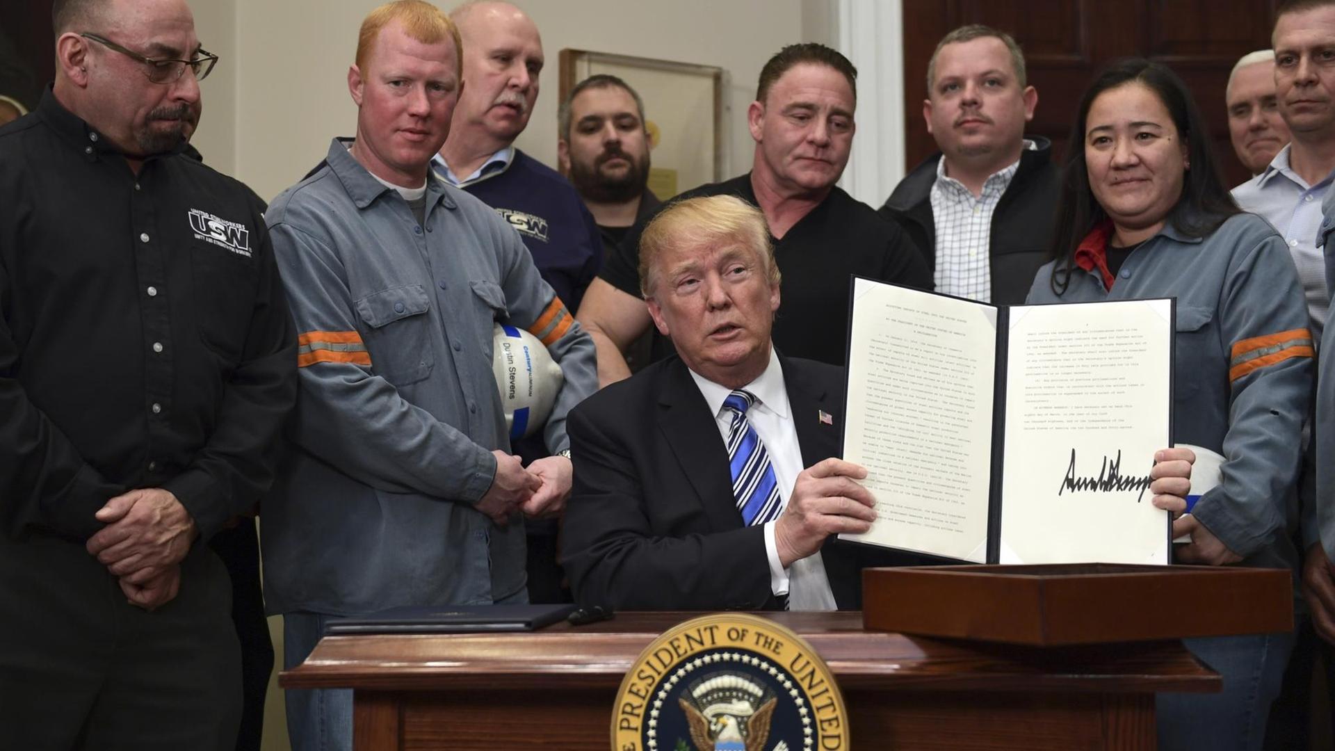 Das Bild zeigt US-Präsident Trump nach der Unterzeichnung seiner Verordnung über Schutzzölle. Er ist umringt von amerikanischen Stahlarbeitern. Das Bild zeigt US-Präsident Trump nach der Unterzeichnung seiner Verordnung über Schutzzölle. Er ist umringt von amerikanischen Stahlarbeitern.