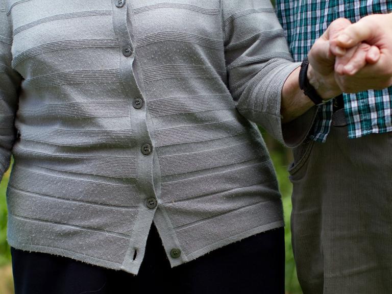 Ein junger Mann geht mit einer Seniorin im Park spazieren.