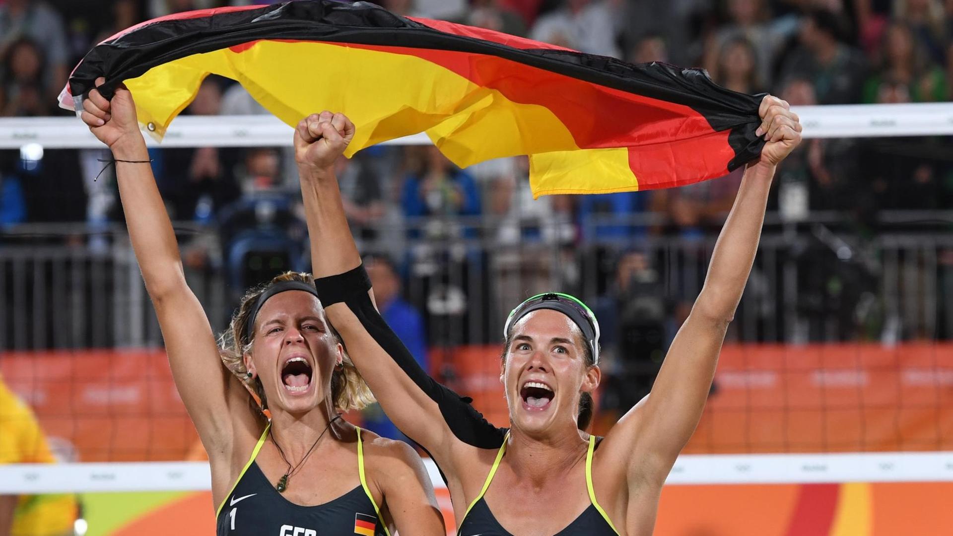Kira Walkenhorst (R) and Laura Ludwig jubeln und schwenken eine Deutschlandflagge, nachdem sie Gold im Beachvolleyball gewonnen haben.