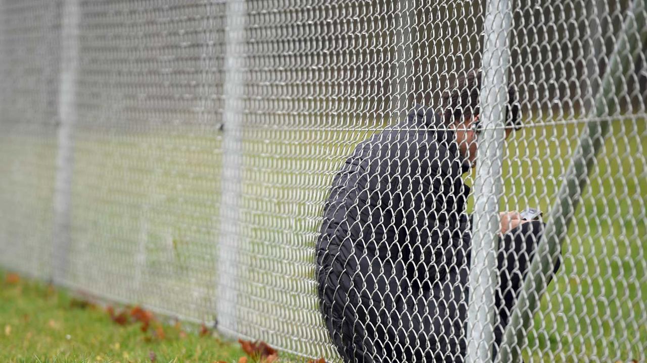 Ein Asylbewerber sitzt am 18.11.2014 in der Erstaufnahmestelle für Flüchtlinge in Meßstetten (Baden-Württemberg) mit seinem Handy hinter einem Zaun.