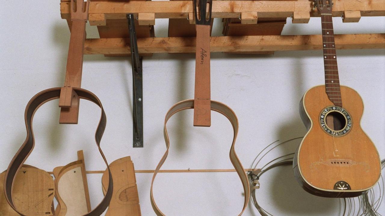 Einzelteile und der Rahmen einer Gitarre hängen in einer Werkstatt an einem Brett.