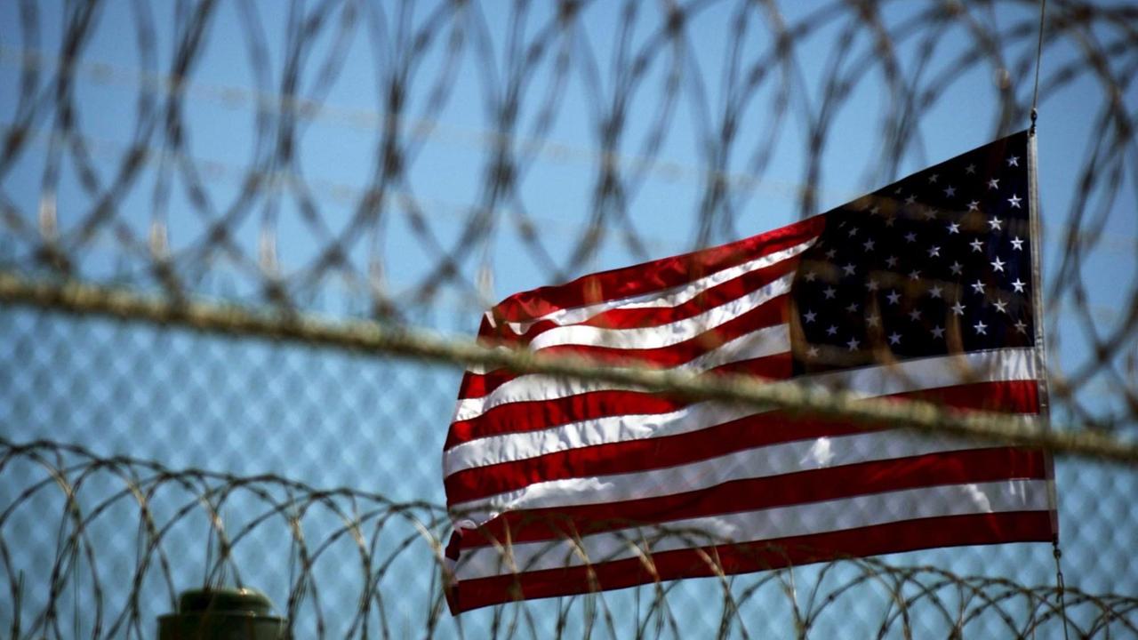 Eine US-Flagge weht hinter einem Stacheldrahtzaun. Eine US-Flagge weht hinter einem Stacheldrahtzaun.