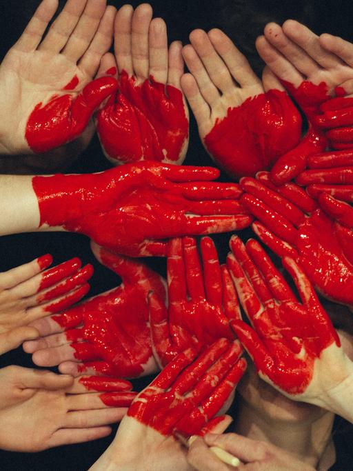Viele Hände formen eine Fläche, auf die mit roter Farbe ein Herz gemalt ist.