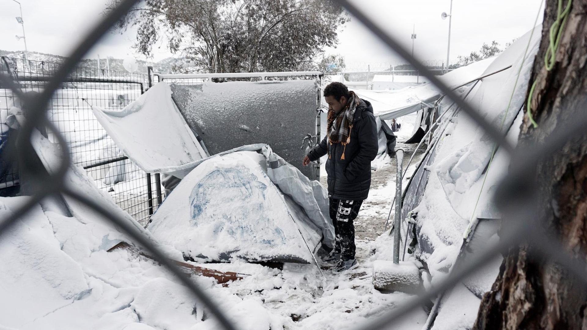 Ein Mann steht vor einem eingeschneiten Iglu-Zelt. Die Kamera blickt durch einen Zaun.