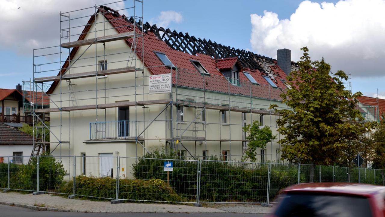 Das Bild zeigt das Haus mit Gerüst schräg von der Seite. Im Vordergrund fährt ein rotes Auto vorbei. Das Bild zeigt das Haus mit Gerüst schräg von der Seite. Im Vordergrund fährt ein rotes Auto vorbei.