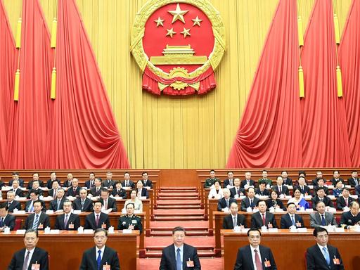 Der Nationalkongress der kommunistischen Partei Chinas in Peking im März 2019. Männer und Frauen sitzen in mehreren Reihen in einem großen Saal.