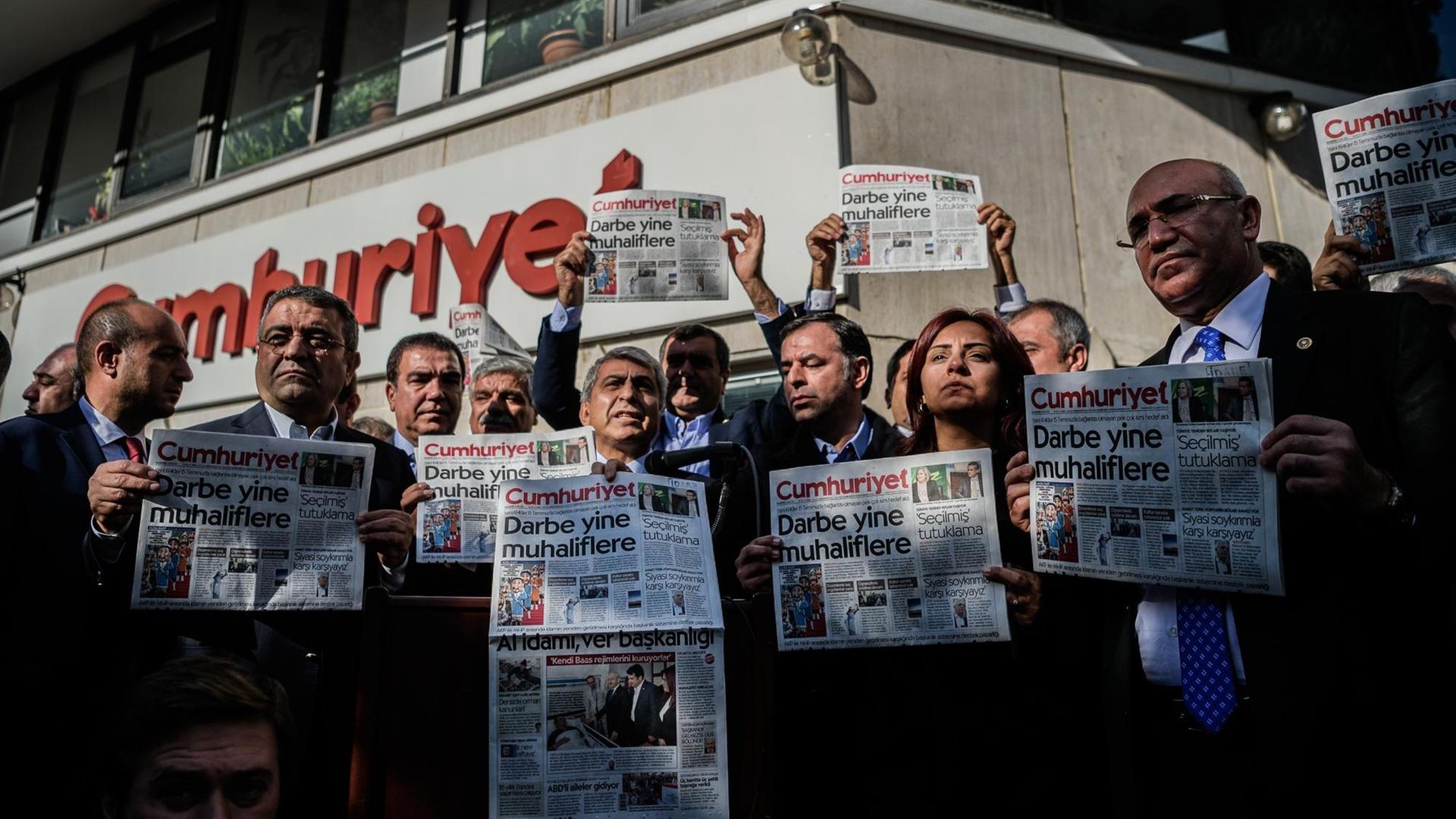 Männer und Frauen stehen vor dem "Cumhuriyet"-Gebäude und halten Ausgaben der Zeitung mit der Aufschrift "Putsch gegen die Opposition" in die Höhe. Männer und Frauen stehen vor dem "Cumhuriyet"-Gebäude und halten Ausgaben der Zeitung mit der Aufschrift "Putsch gegen die Opposition" in die Höhe.