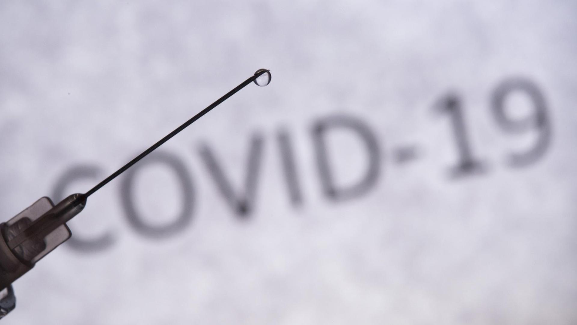 Das Foto zeigt eine Spritze und im Hintergrund den Schriftzug COVID-19 Das Foto zeigt eine Spritze und im Hintergrund den Schriftzug COVID-19