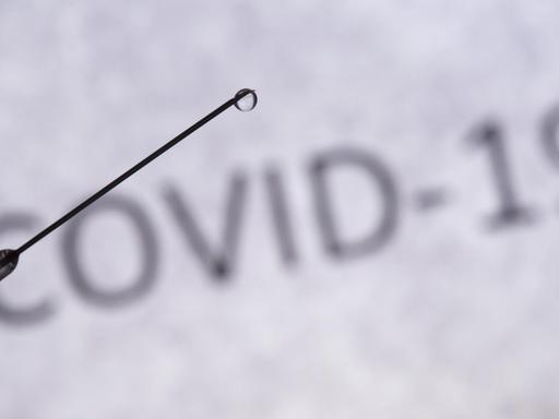 Das Foto zeigt eine Spritze und im Hintergrund den Schriftzug COVID-19