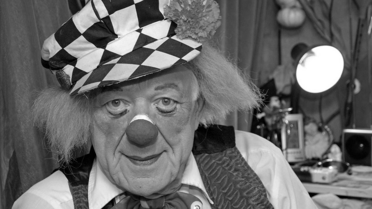 Popow blickt in voller Clownsmonitur und mit geschminktem Gesicht freundlich lächelnd in die Kamera. Popow blickt in voller Clownsmonitur und mit geschminktem Gesicht freundlich lächelnd in die Kamera.