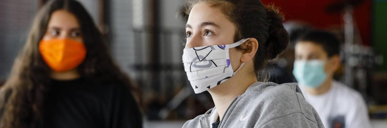 In einem Klassenzimmer sitzen zwei Schülerinnen und ein Schüler mit Mundschutz. In einem Klassenzimmer sitzen zwei Schülerinnen und ein Schüler mit Mundschutz.