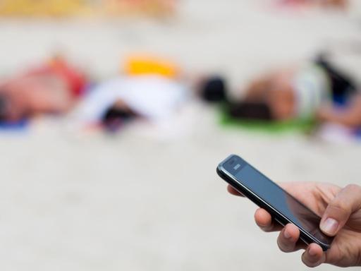 Eine Frau schreibt am 04.08.2013 mit einem Mobiltelefon eine SMS am Strand von Kolberg, Polen, an der Ostsee.