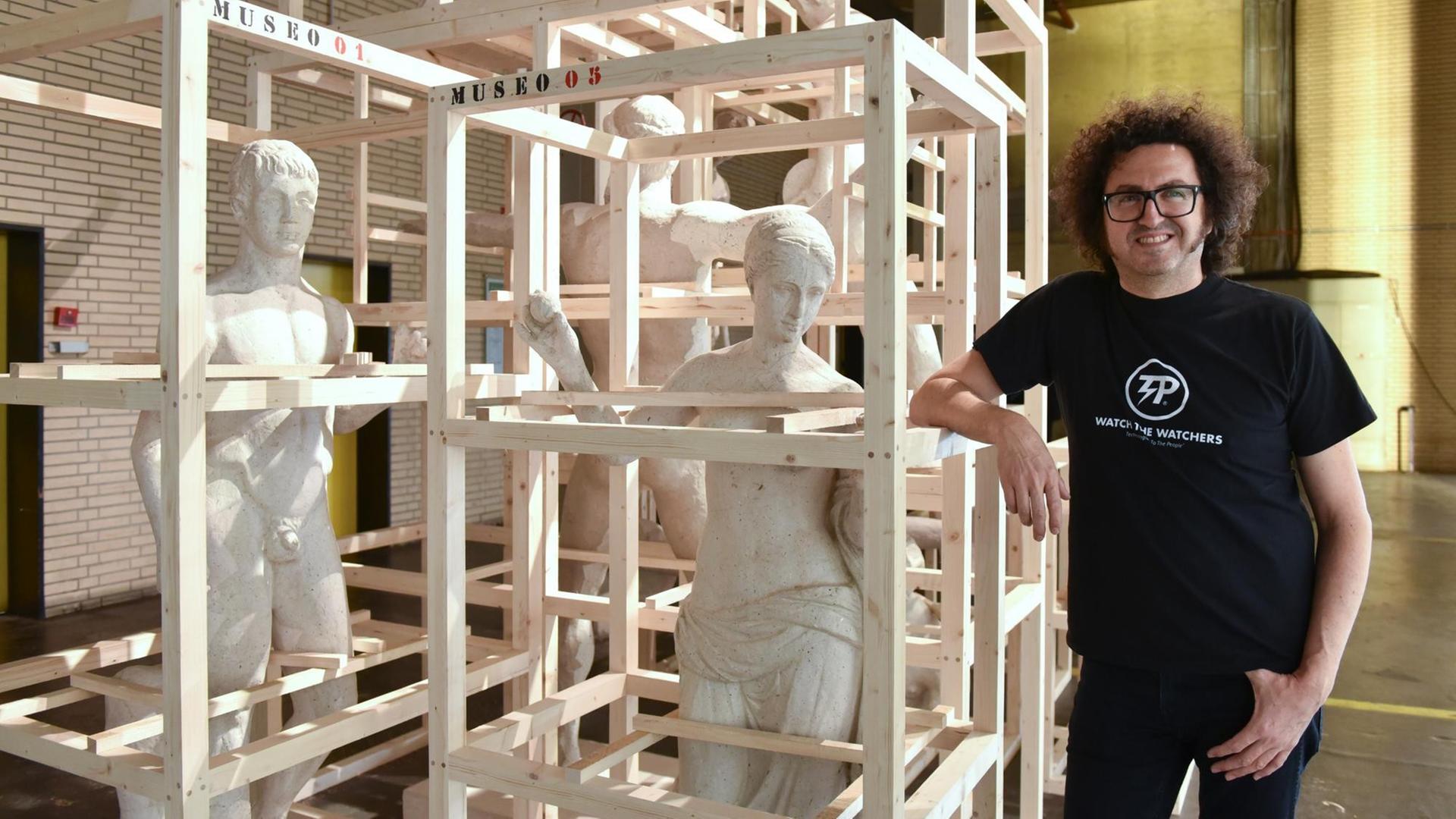 Der Künstler steht neben einem Kunst-Werk aus Menschen-Figuren und Latten-Gerüsten. Der Künstler steht neben einem Kunst-Werk aus Menschen-Figuren und Latten-Gerüsten.