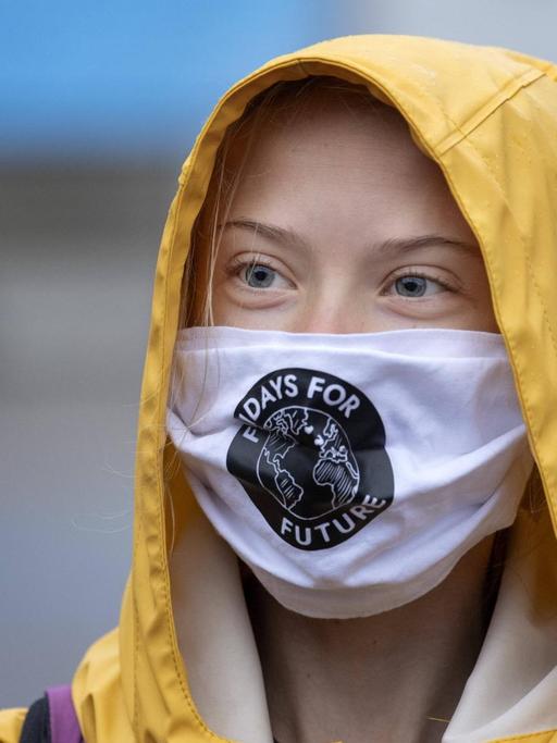 Porträt der schwedischen Klimaaktivistin Greta Thunberg mit Mund-Nasen-Schutz und gelber Regenmantel-Kapuze.