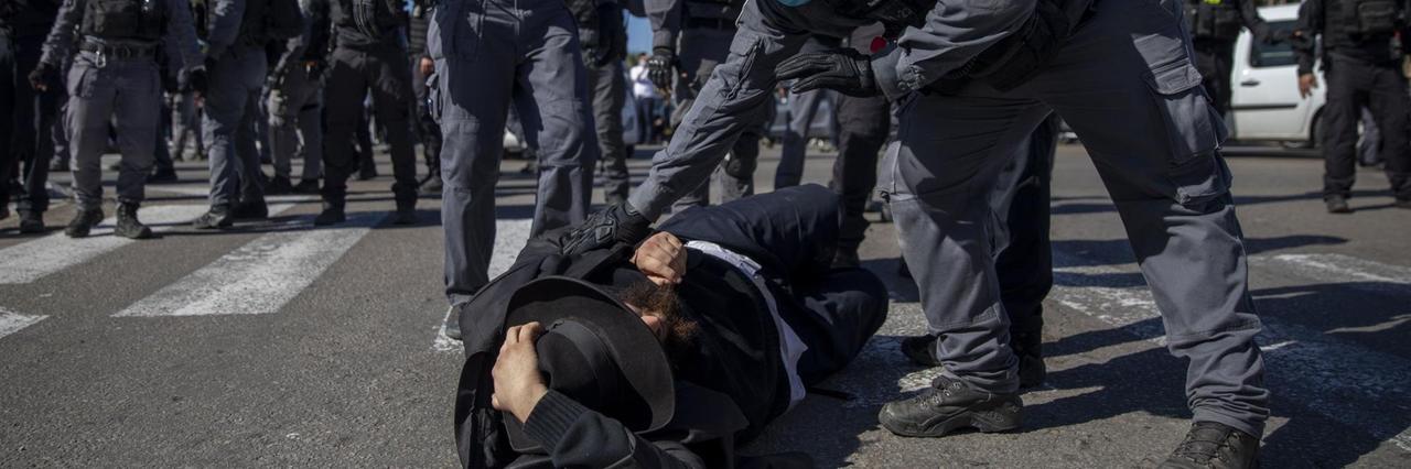Israelische Polizisten halten einen ultra-orthodoxen Juden am Boden fest.
