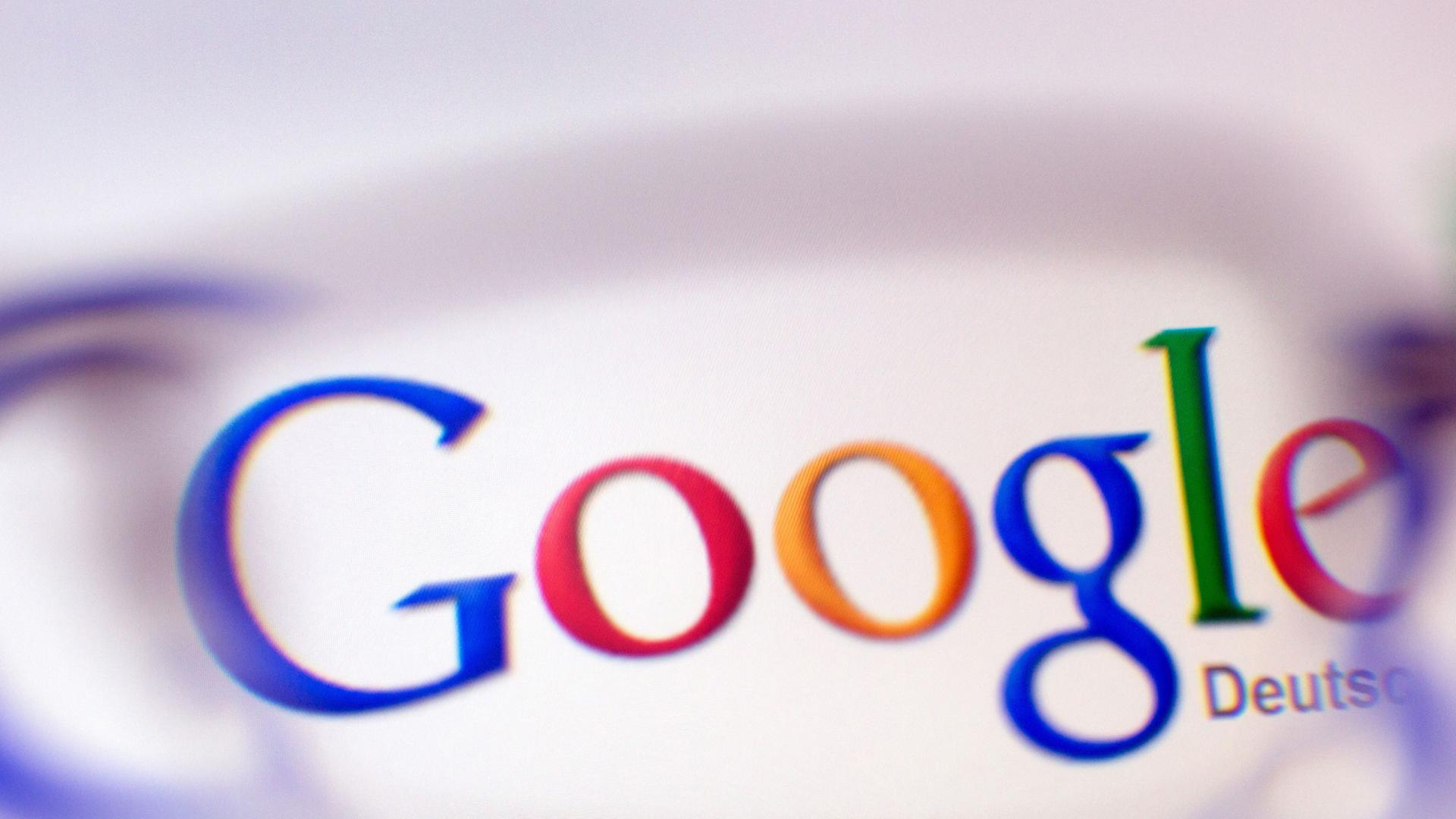 Das Google-Logo ist durch ein Brillenglas auf einem Bildschirm zu sehen. Das Google-Logo ist durch ein Brillenglas auf einem Bildschirm zu sehen.