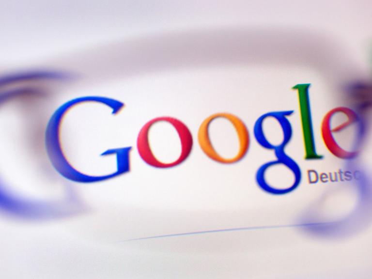 Das Google-Logo ist durch ein Brillenglas auf einem Bildschirm zu sehen.