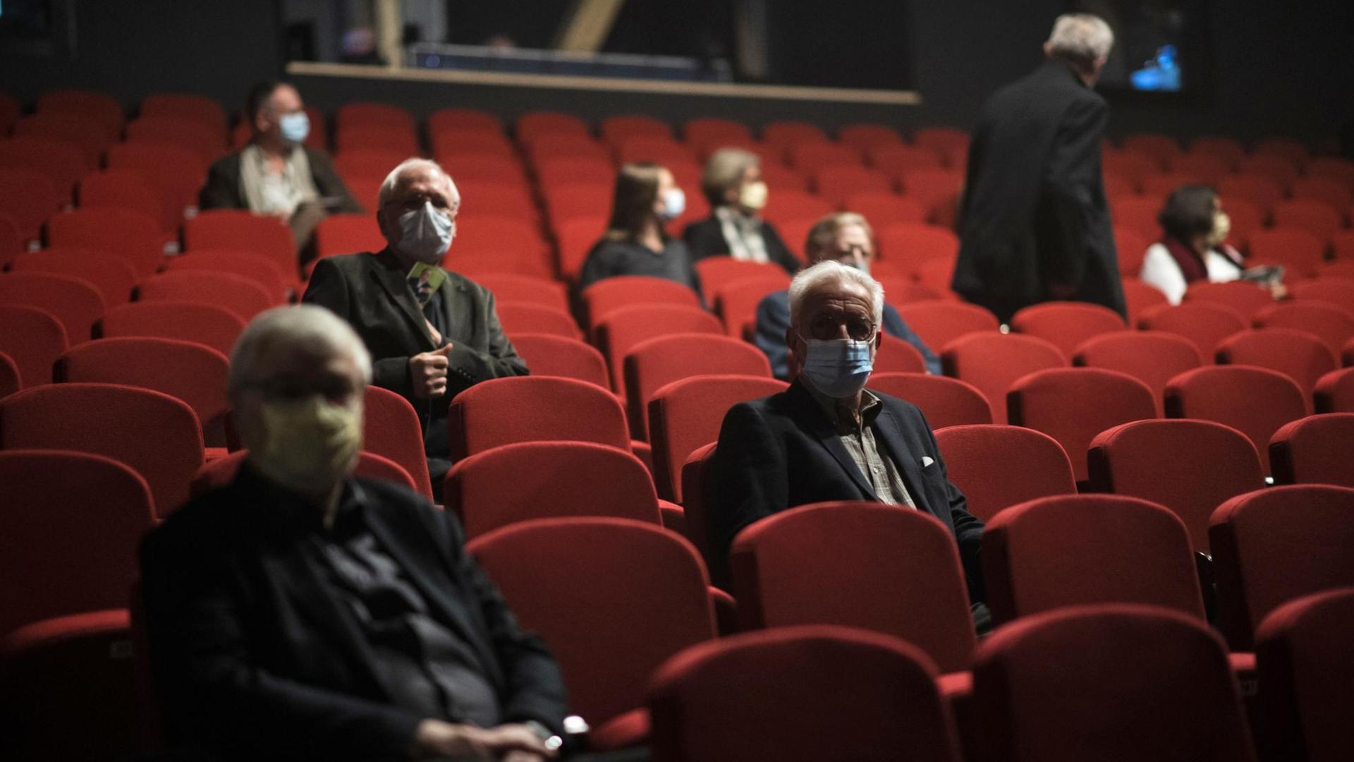 Menschen mit Schutzmasken sitzen im Theatersaal. Menschen mit Schutzmasken sitzen im Theatersaal.