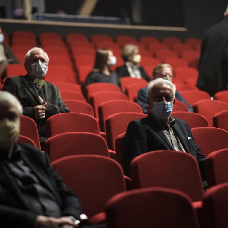 Menschen mit Schutzmasken sitzen im Theatersaal.