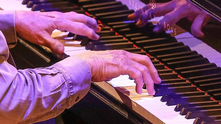 Die Hände des Pianisten Bobo Stenson spielen Klavier und spiegeln sich dabei im Lack des Flügels.