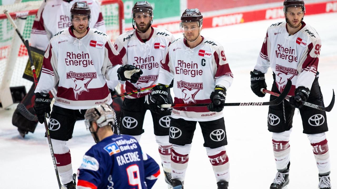 Vier Spieler der Kölner Haie stehen in einer Reihe und schützen das Tor vor einem Spieler der Iserlohn Roosters. Vier Spieler der Kölner Haie stehen in einer Reihe und schützen das Tor vor einem Spieler der Iserlohn Roosters.