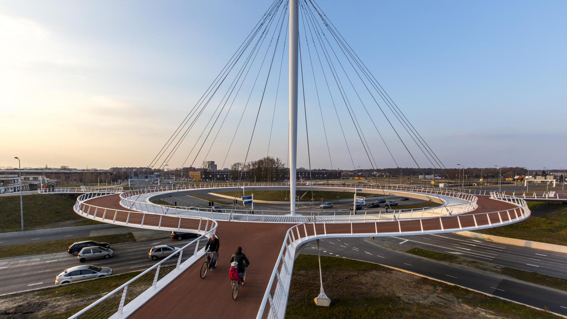 Ein futuristischer Bau in Form eines Kreisels für Fahrradfahrer schwebt über einer Autostraßenkreuzung. Ein futuristischer Bau in Form eines Kreisels für Fahrradfahrer schwebt über einer Autostraßenkreuzung.