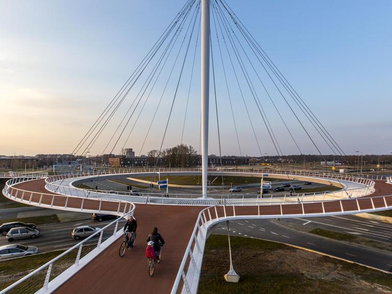 Ein futuristischer Bau in Form eines Kreisels für Fahrradfahrer schwebt über einer Autostraßenkreuzung.