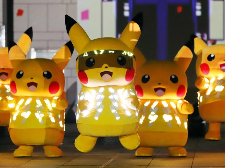 Fünf menschengroße Pikachus (ein gelbes. hasenähnliches Wesen mit langen Ohren, die an der Spitze schwarz sind) mit LED-Lichtern tanzen auf einer Bühne.
