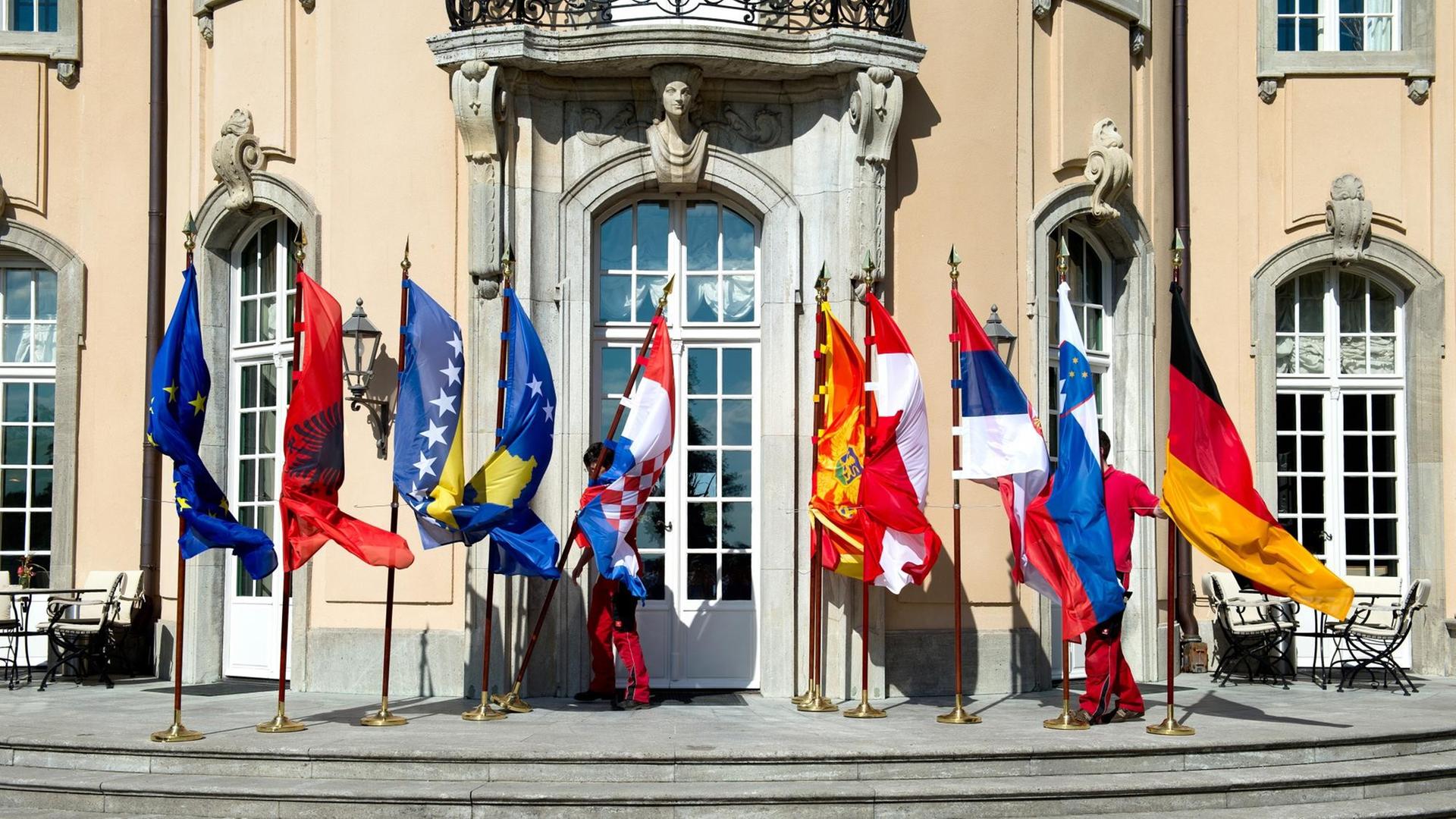 Mitarbeiter des Auswärtigen Amts mühen sich bei der Westbalkan-Konferenz in Berlin vor dem Gruppenbild der Außenminister mit den wehenden Fahnen, die umzukippen drohen. Mitarbeiter des Auswärtigen Amts mühen sich bei der Westbalkan-Konferenz in Berlin vor dem Gruppenbild der Außenminister mit den wehenden Fahnen, die umzukippen drohen.