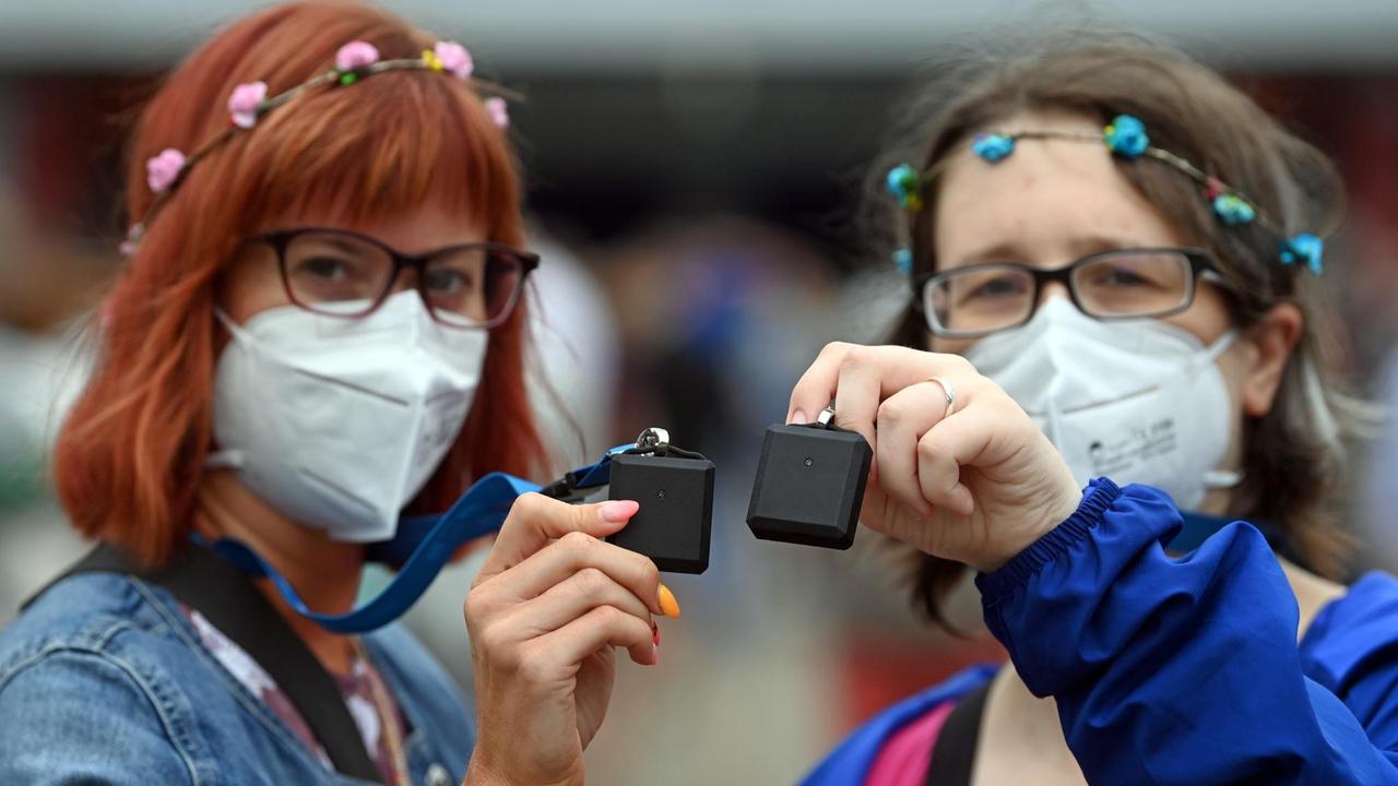 22.08.2020, Sachsen, Leipzig: Franziska Brauer (l) und Doreen Linke, Probandinnen aus Sachsen und Sachsen-Anhalt, zeigen sogenannte "Tracer", die bei dem Großversuch der Universitätsmedizin Halle/Saale eingesetzt werden und Wege verfolgen können. Rund 1400 Besucher beteiligen sich an dem Versuch unter dem Titel «Restart-19», bei dem der Popsänger Tim Bendzko auftritt. Die Wissenschaftler wollen mit Sensoren und anderen Hilfsmitteln Laufwege überwachen und fluoreszierendes Desinfektionsmittel soll sichtbar machen, welche Flächen oft angefasst werden. Auch der Flug der Aerosole - kleinste Partikel-Mischungen, die das Virus tragen könnten - soll nachvollzogen werden. Ziel ist ein mathematisches Modell, mit dem das Risiko eines Coronaausbruchs nach einer Großveranstaltung in einer Halle bewertet werden kann. Foto: Hendrik Schmidt/dpa-Zentralbild/dpa | Verwendung weltweit 22.08.2020, Sachsen, Leipzig: Franziska Brauer (l) und Doreen Linke, Probandinnen aus Sachsen und Sachsen-Anhalt, zeigen sogenannte "Tracer", die bei dem Großversuch der Universitätsmedizin Halle/Saale eingesetzt werden und Wege verfolgen können. Rund 1400 Besucher beteiligen sich an dem Versuch unter dem Titel «Restart-19», bei dem der Popsänger Tim Bendzko auftritt. Die Wissenschaftler wollen mit Sensoren und anderen Hilfsmitteln Laufwege überwachen und fluoreszierendes Desinfektionsmittel soll sichtbar machen, welche Flächen oft angefasst werden. Auch der Flug der Aerosole - kleinste Partikel-Mischungen, die das Virus tragen könnten - soll nachvollzogen werden. Ziel ist ein mathematisches Modell, mit dem das Risiko eines Coronaausbruchs nach einer Großveranstaltung in einer Halle bewertet werden kann. Foto: Hendrik Schmidt/dpa-Zentralbild/dpa | Verwendung weltweit