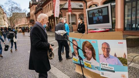 Ein Mann steht auf dem Wochenmarkt und spricht via Zoom-Konferenz mit den drei Mainzer CDU-Direktkandidaten zur Landtagswahl 2021.