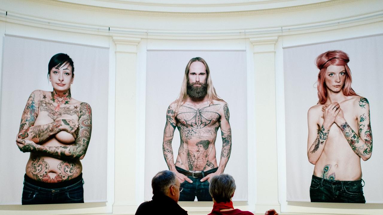 Ein Mann und eine Frau schauen sich in Hamburg im Museum für Kunst und Gewerbe (MKG) in der Ausstellung "Tattoo" Bilder von Tätowierten vom Fotografen Ralf Mitsch an. Ein Mann und eine Frau schauen sich in Hamburg im Museum für Kunst und Gewerbe (MKG) in der Ausstellung "Tattoo" Bilder von Tätowierten vom Fotografen Ralf Mitsch an.