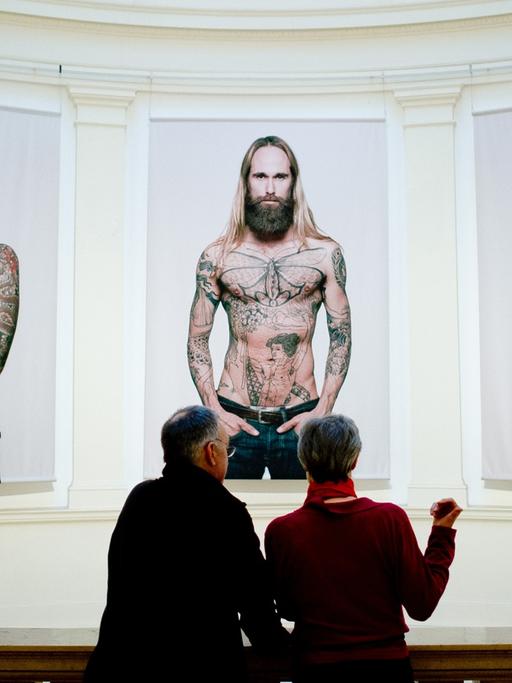 Ein Mann und eine Frau schauen sich in Hamburg im Museum für Kunst und Gewerbe (MKG) in der Ausstellung "Tattoo" Bilder von Tätowierten vom Fotografen Ralf Mitsch an.