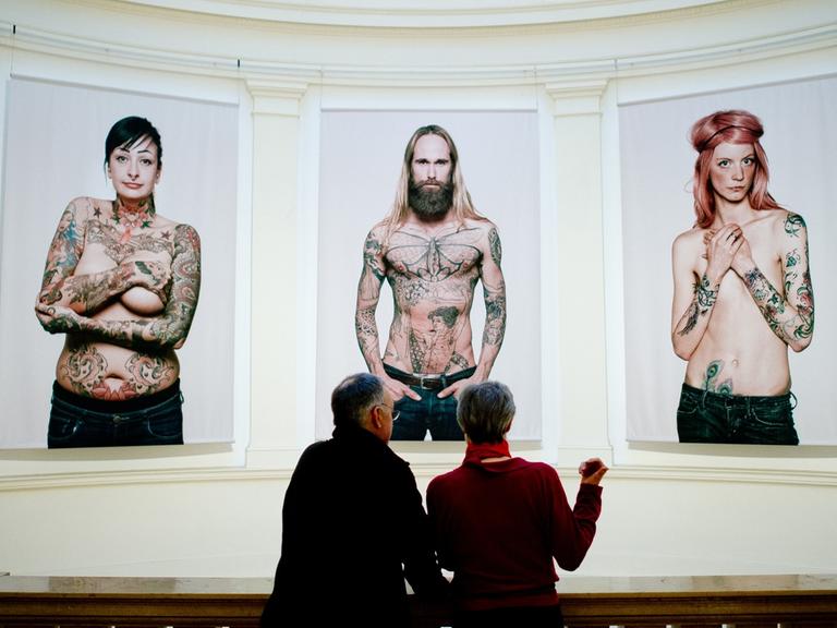 Ein Mann und eine Frau schauen sich in Hamburg im Museum für Kunst und Gewerbe (MKG) in der Ausstellung "Tattoo" Bilder von Tätowierten vom Fotografen Ralf Mitsch an.