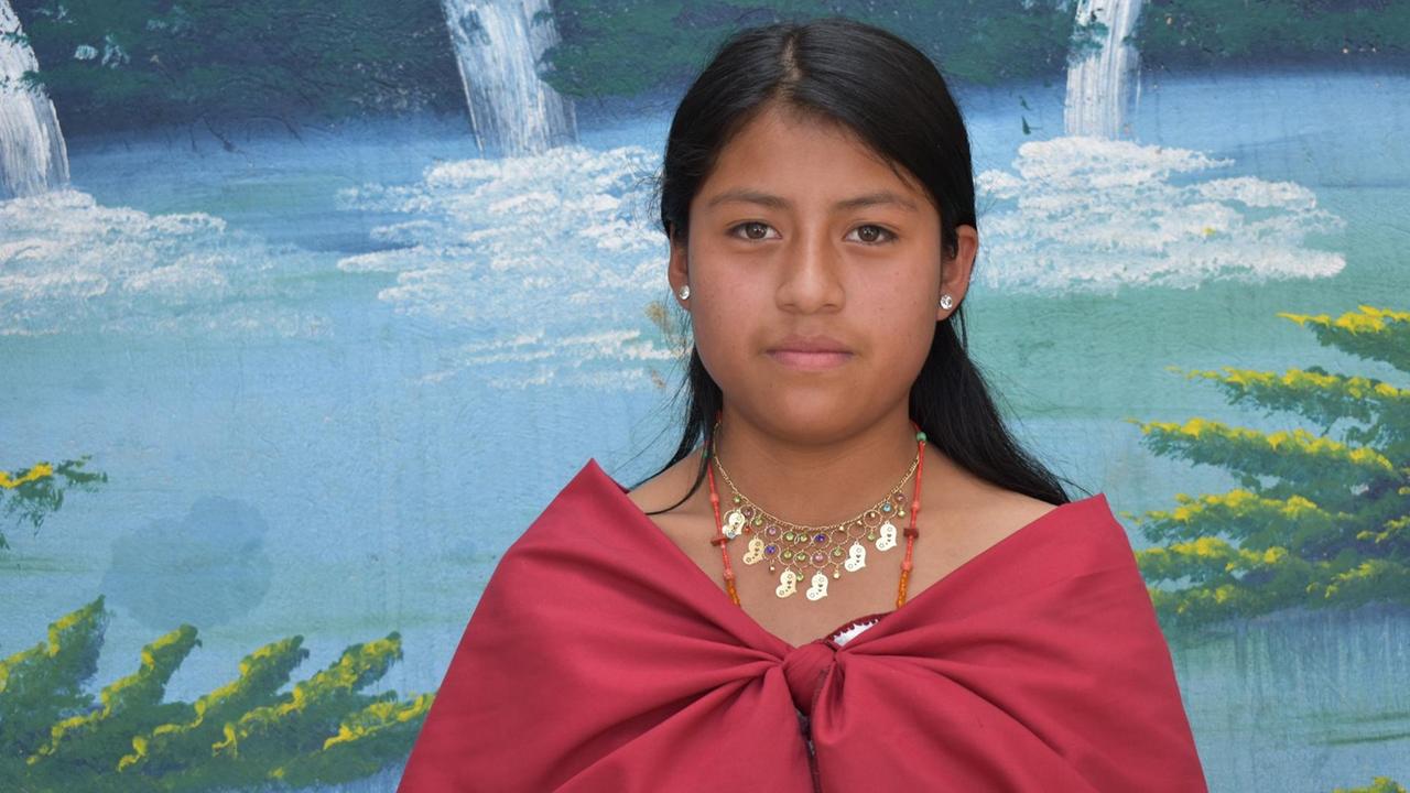 Jennifer Quispe steht in einem roten Kleid vor dem Wandbild eines Sees. Jennifer Quispe steht in einem roten Kleid vor dem Wandbild eines Sees.
