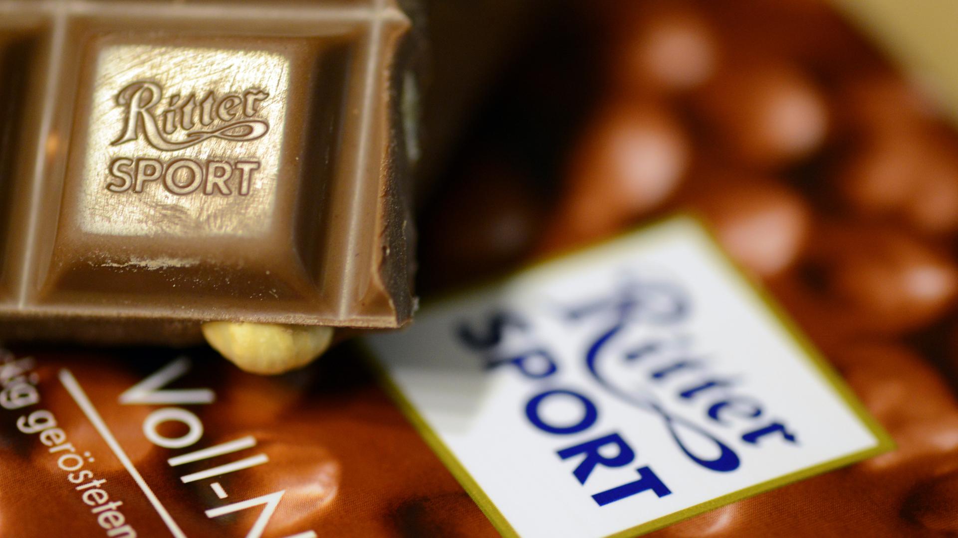 Das Bild zeigt ein kleines Stück Voll-Nuss-Schokolade der Marke Ritter-Sport. Es liegt auf einer Verpackung der Schokoladentafel. Das Bild zeigt ein kleines Stück Voll-Nuss-Schokolade der Marke Ritter-Sport. Es liegt auf einer Verpackung der Schokoladentafel.