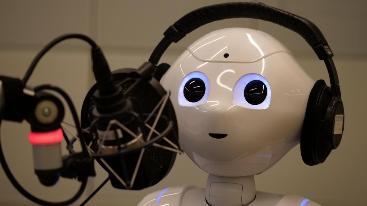 Ein weißer Roboterkopf mit großen Augen schaut hinter einem Mikroophon hervor