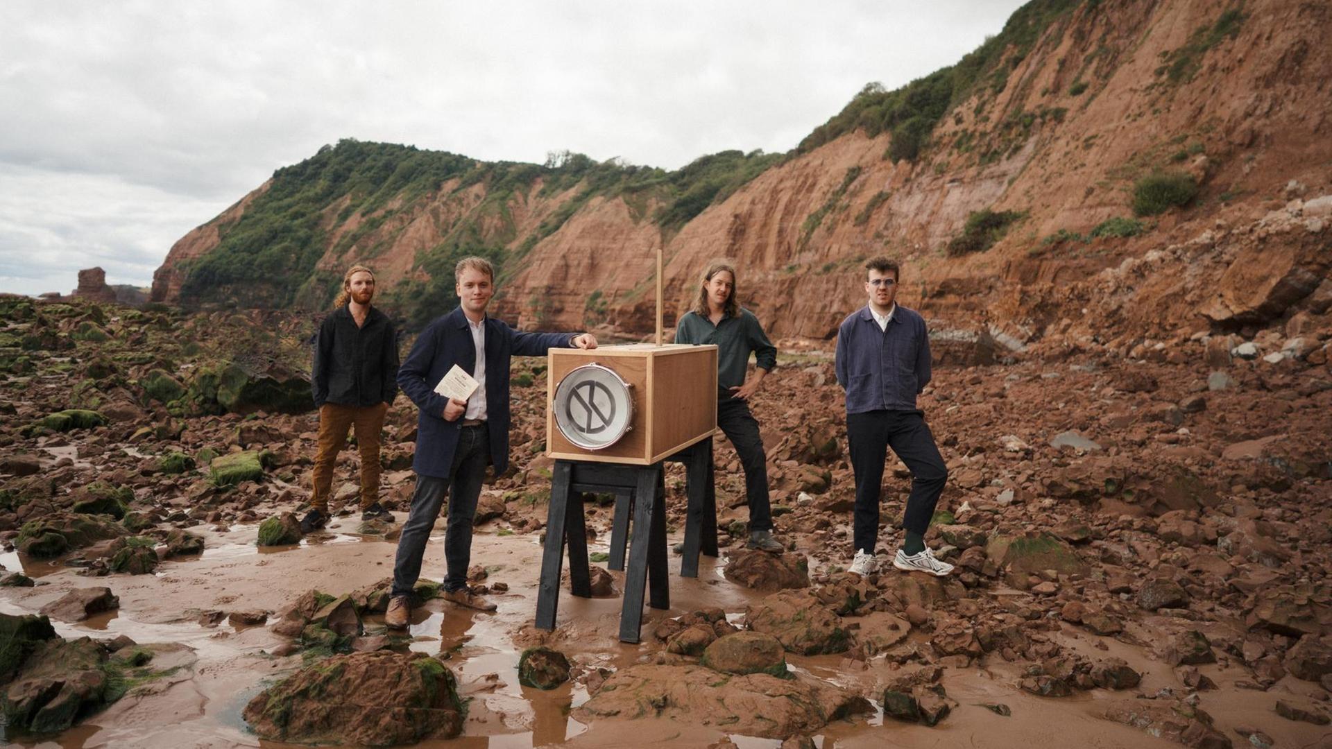 Die Band Bristol steht mit einer überdimensional großen Plattenkamera in einem Steinbruch