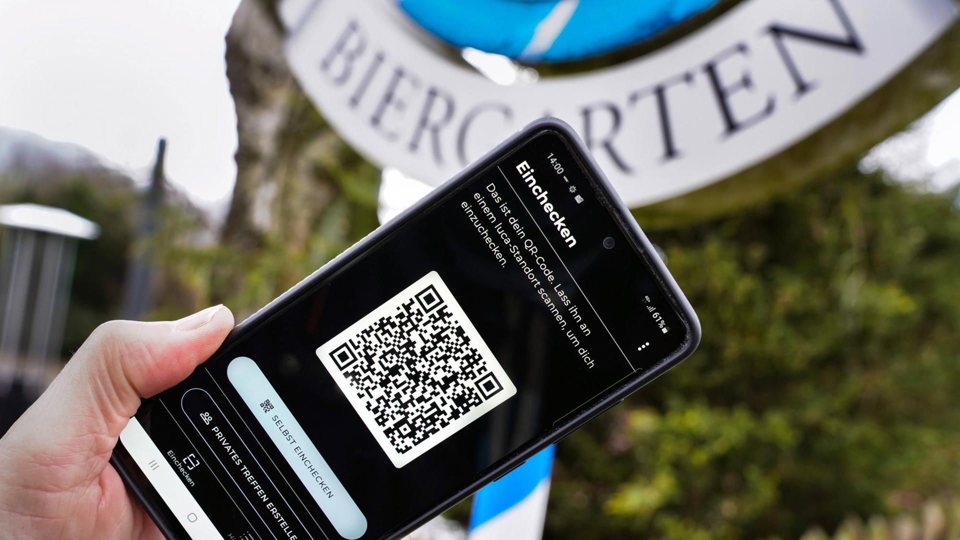 Luca-App mit QR-Code auf einem Smartphone vor einem Biergartenschild. Luca-App mit QR-Code auf einem Smartphone vor einem Biergartenschild.