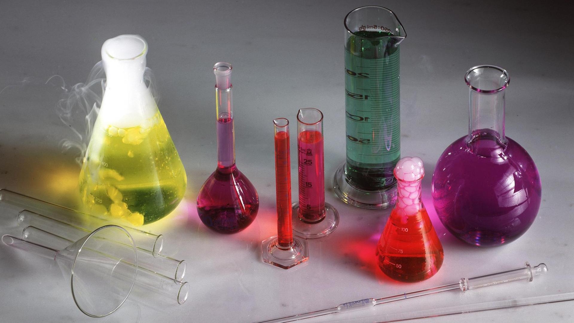 Laborgefäße, wie Glaskolben und Messzylinder, mit verschiedenfarbigen Flüssigkeiten