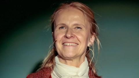 Cornelia Funke vor grünlichem Hintergrund, bei einer Lesung.