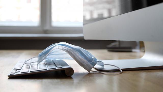 Arbeitsplatz: Rechner und Tastatur mit Atemschutzmaske, Symbolfoto
