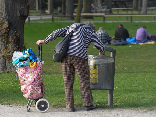 Eine alte Frau sammelt Pfandflaschen aus einem Mülleimer.