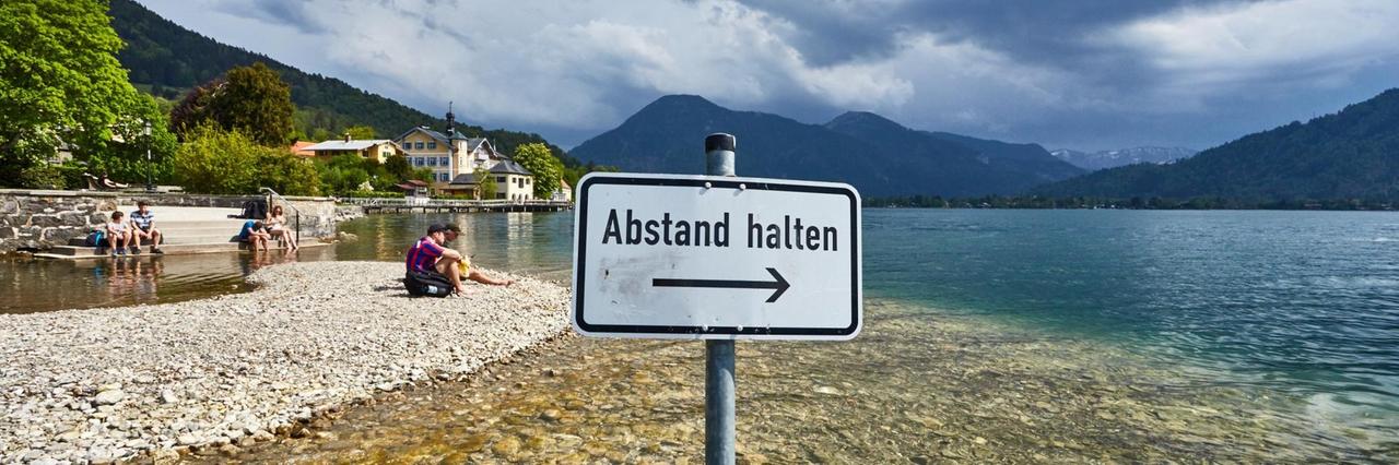 Ein Schild mit der Aufschrift "Abstand halten" an einem idyllischen See. Ein Schild mit der Aufschrift "Abstand halten" an einem idyllischen See.